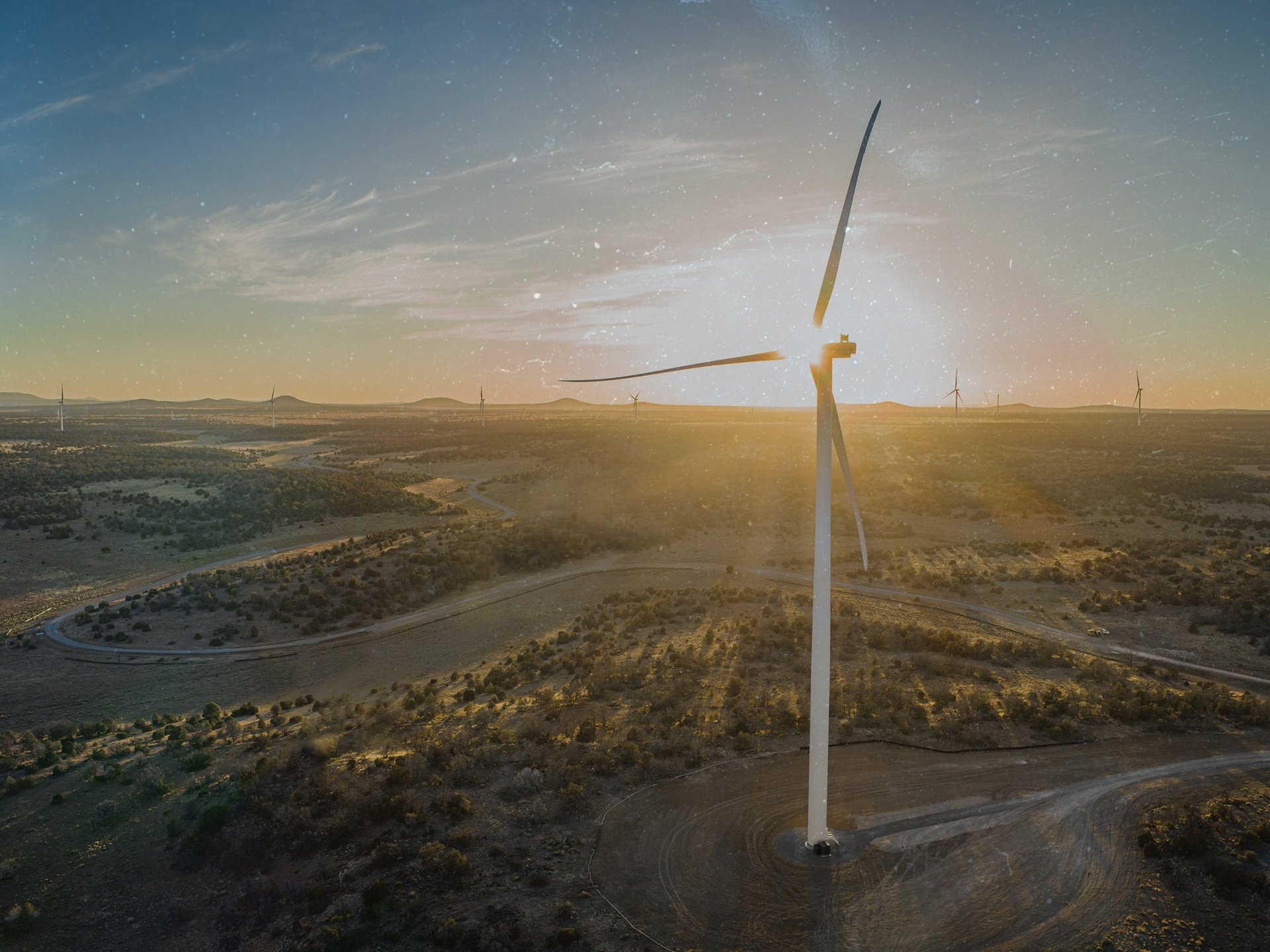 drone image of a wind turbine project with a prominent turbine in the front silhouetted in the rising sun