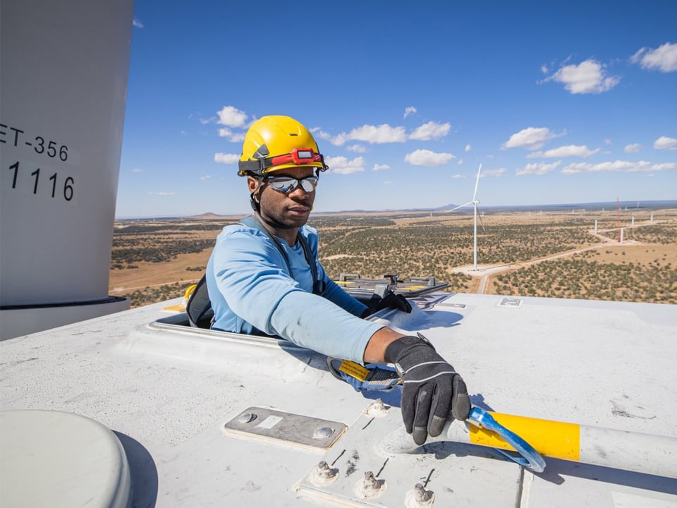 Male construction worker working partly within body of wind turbine and with torso outside working on top of turbine