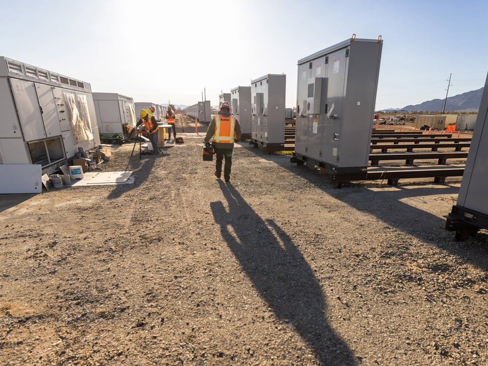 Three electrical workers get to work on large electrical components for a solar project early in the morning as the sun is coming up