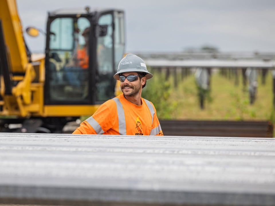 close up of a solar worker in a gray hat working on a solar project with machinery in the background