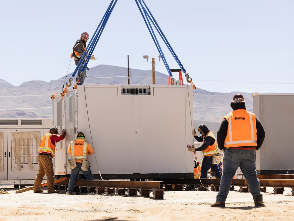 Multiple employees placing large electronic component in place with crane