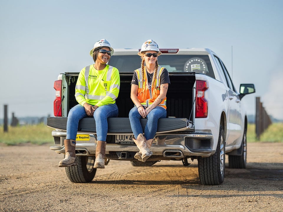 Two female workers sitting on truck tailgate laughing