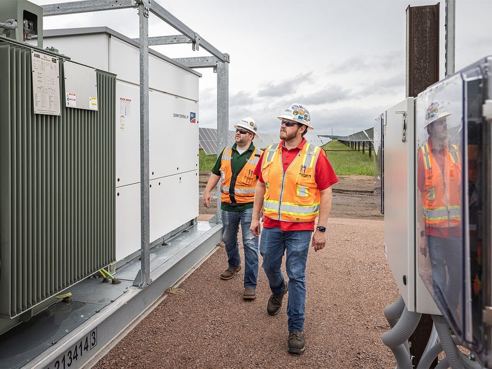 Site leaders looking at an inverter at a solar project