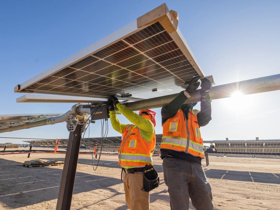 Two field workers install a solar panel