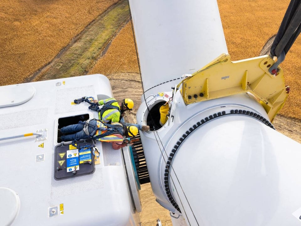 Overhead drone shot of a two man team of wind turbine climbers completing the connection of the nacelle to the blade system